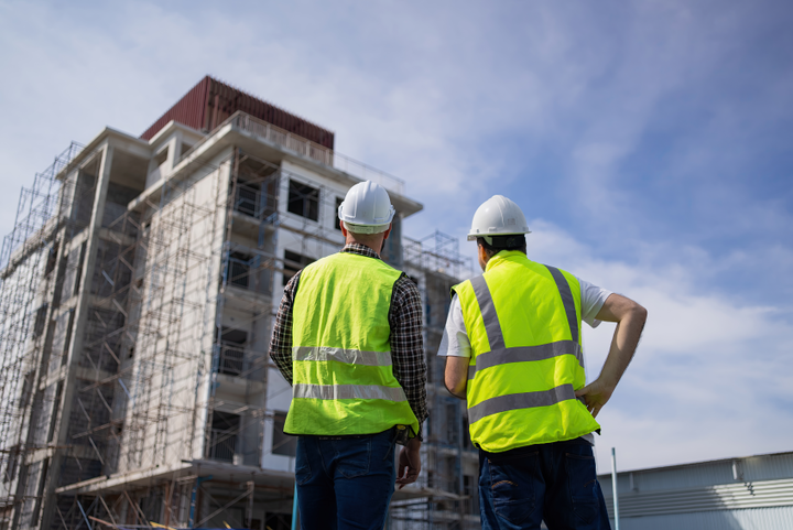 Two construction workers wearing yellow reflective vests looking at a building under construction